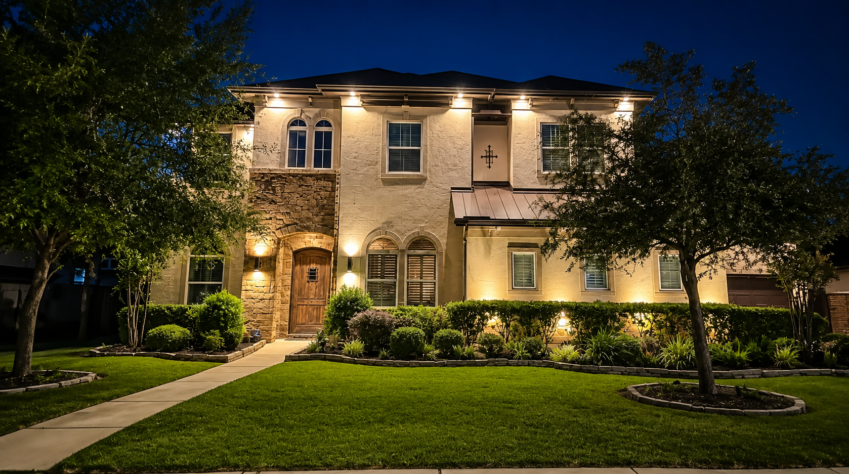 Professionally installed warm, white LED landscape Lighting, illuminating the front of a two-story home, highlighting architectural features, walkways, trees, and landscaping to improve curb, appeal, safety, and nighttime visibility.