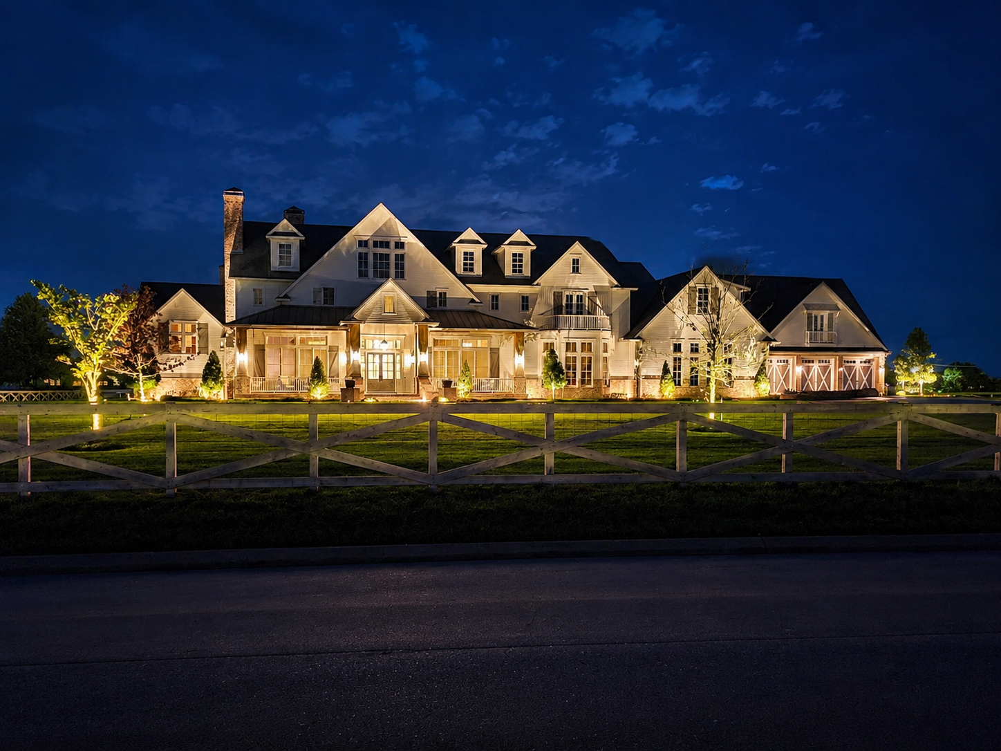 Large custom home illuminated with professionally installed LED landscape lighting, highlighting architectural features, trees, walkways, and the front entrance at night.
