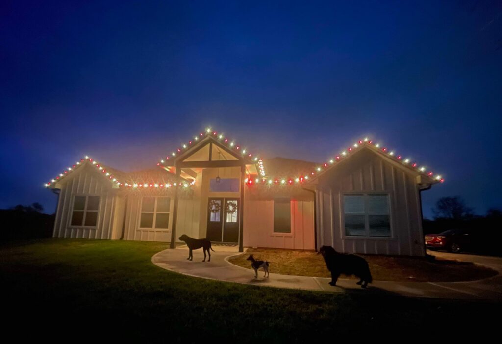 Professional custom C9 LED Christmas lights installed along the roofline of a modern home at dusk, creating a bright, festive holiday display with a warmly illuminated front entrance.